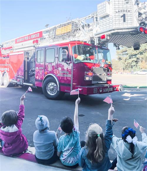 Kids with flags waving at firetruck parading through the school parking lot